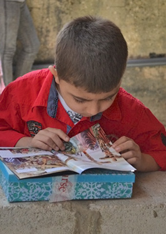 A Syrian child eagerly reads one of the children's Bible stories received during a distribution to refugees.