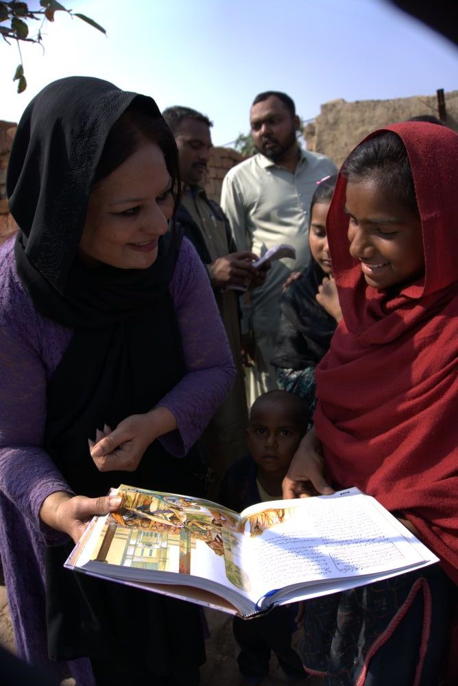 A girl receiving a children's Bible from a Pakistani gospel worker in early 2026.