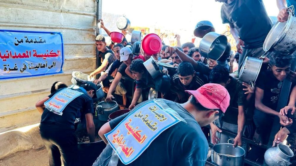 Workers in Gaza hand out hot food below a sign saying it is provided by a local church.
