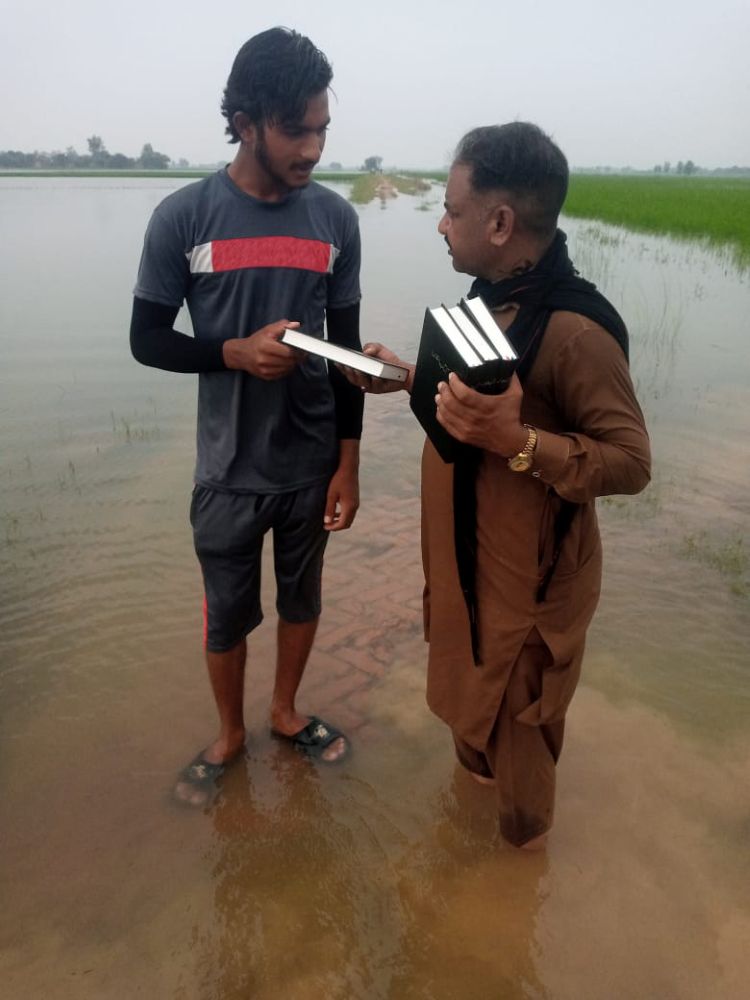 A Pakistani Christian hands out Bibles along a flooded road.